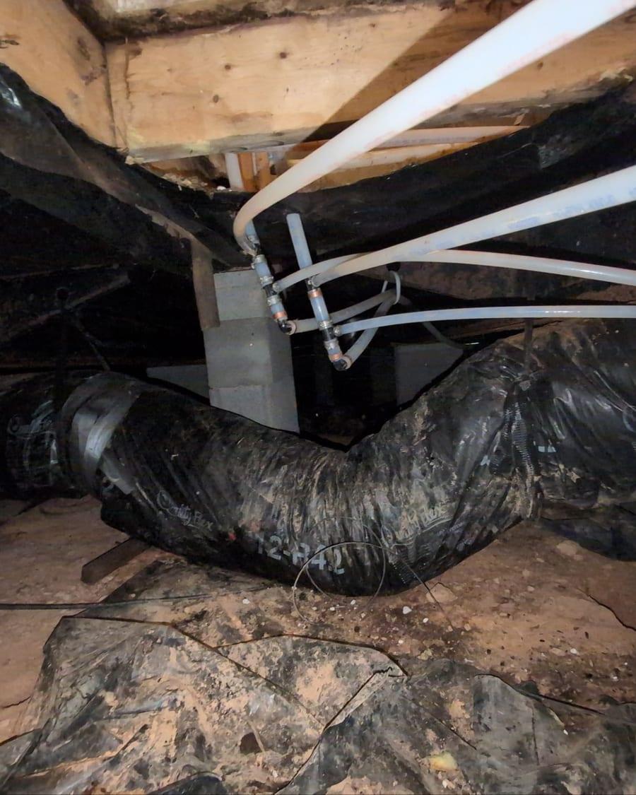 Ductwork and a torn vapor barrier in a crawl space
