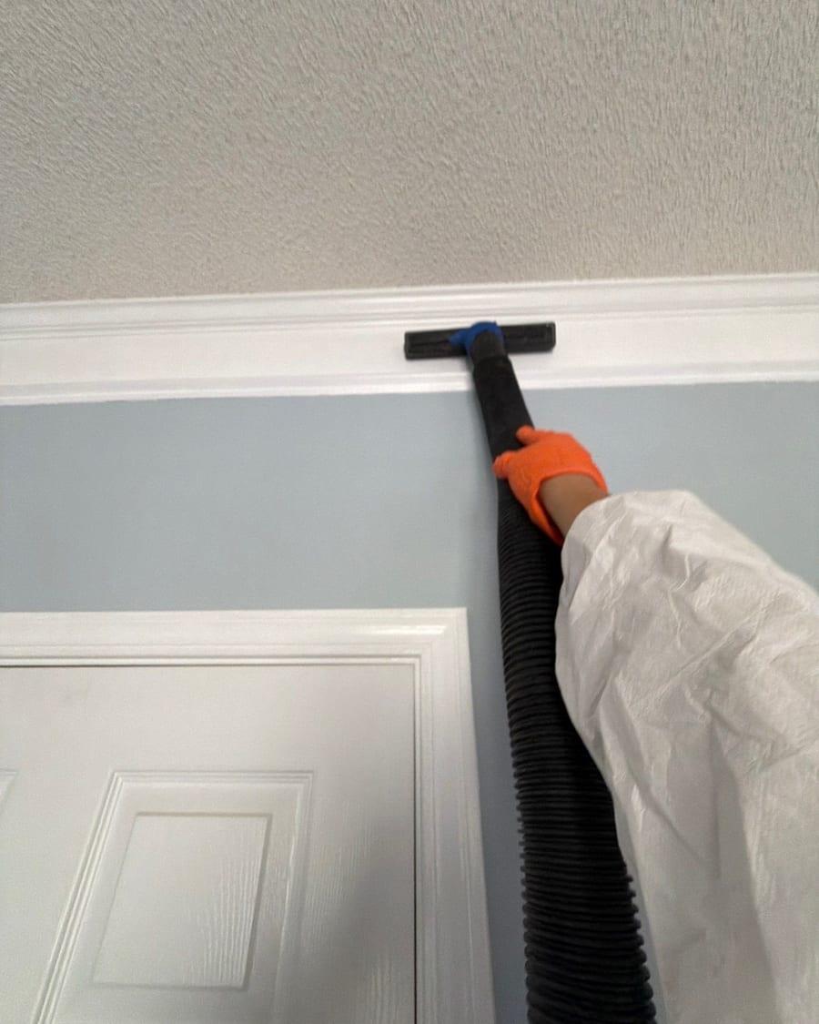 A gloved hand cleaning crown moulding with a HEPA vacuum