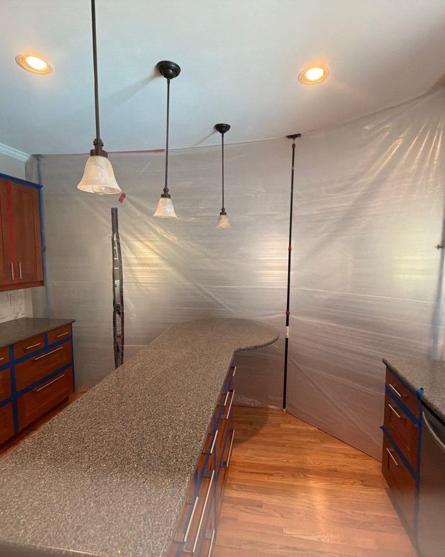 A kitchen sealed off with plastic sheeting and taped cabinets before work starts