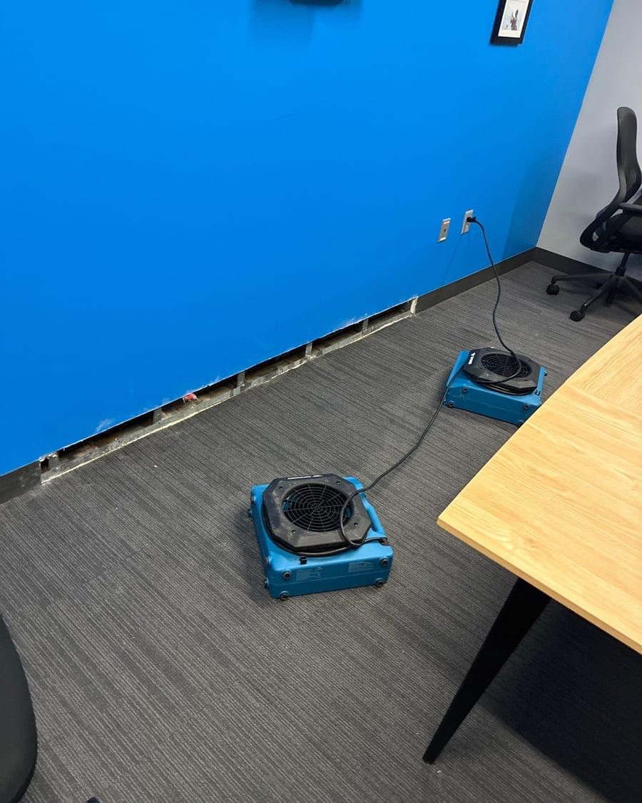 Air movers drying an office after the bottom of the wall was cut away