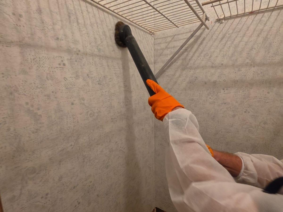 A technician in protective gear cleaning a surface with a HEPA vacuum