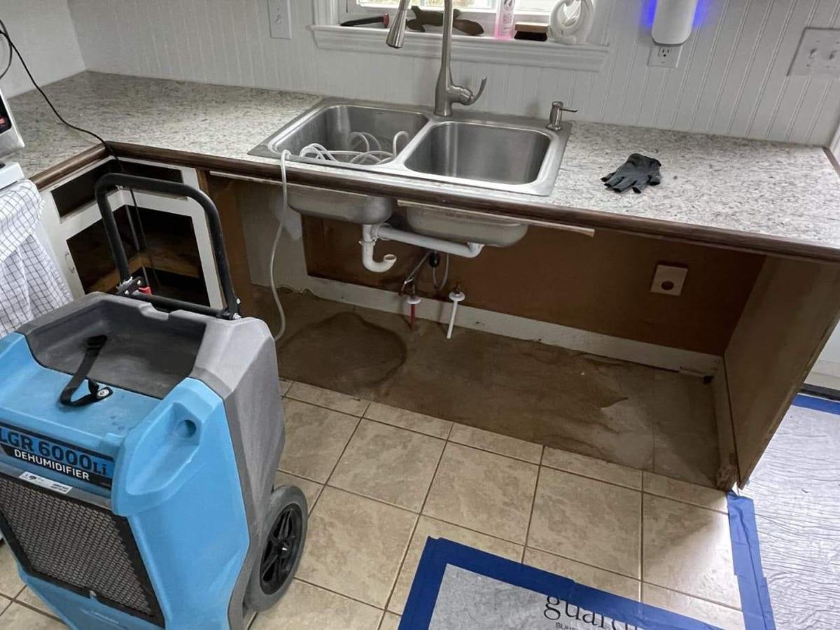 A kitchen sink cabinet opened up and drying after a leak