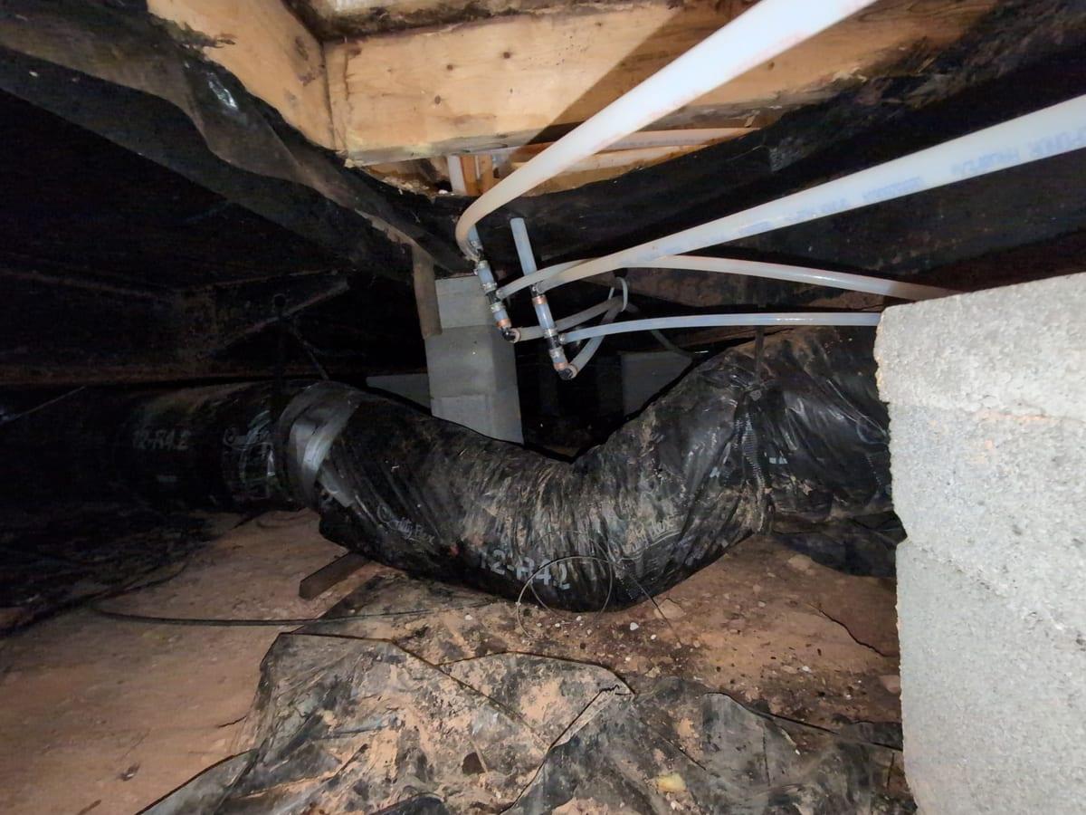 Ductwork and a torn vapor barrier in a crawl space