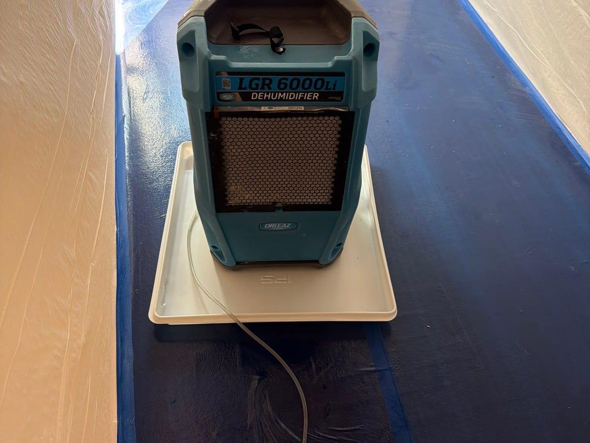 A dehumidifier running on floor protection in a hallway