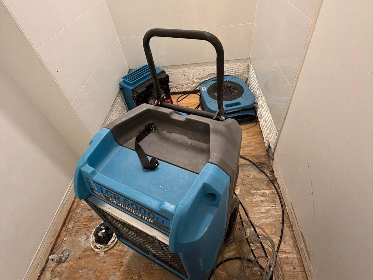 Air movers and a dehumidifier drying a bathroom after the damaged floor came out