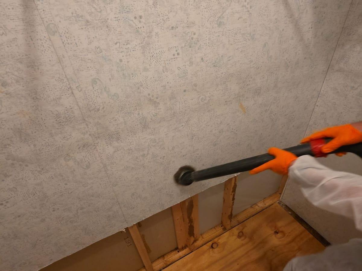 A technician in protective gear HEPA-vacuuming a wall