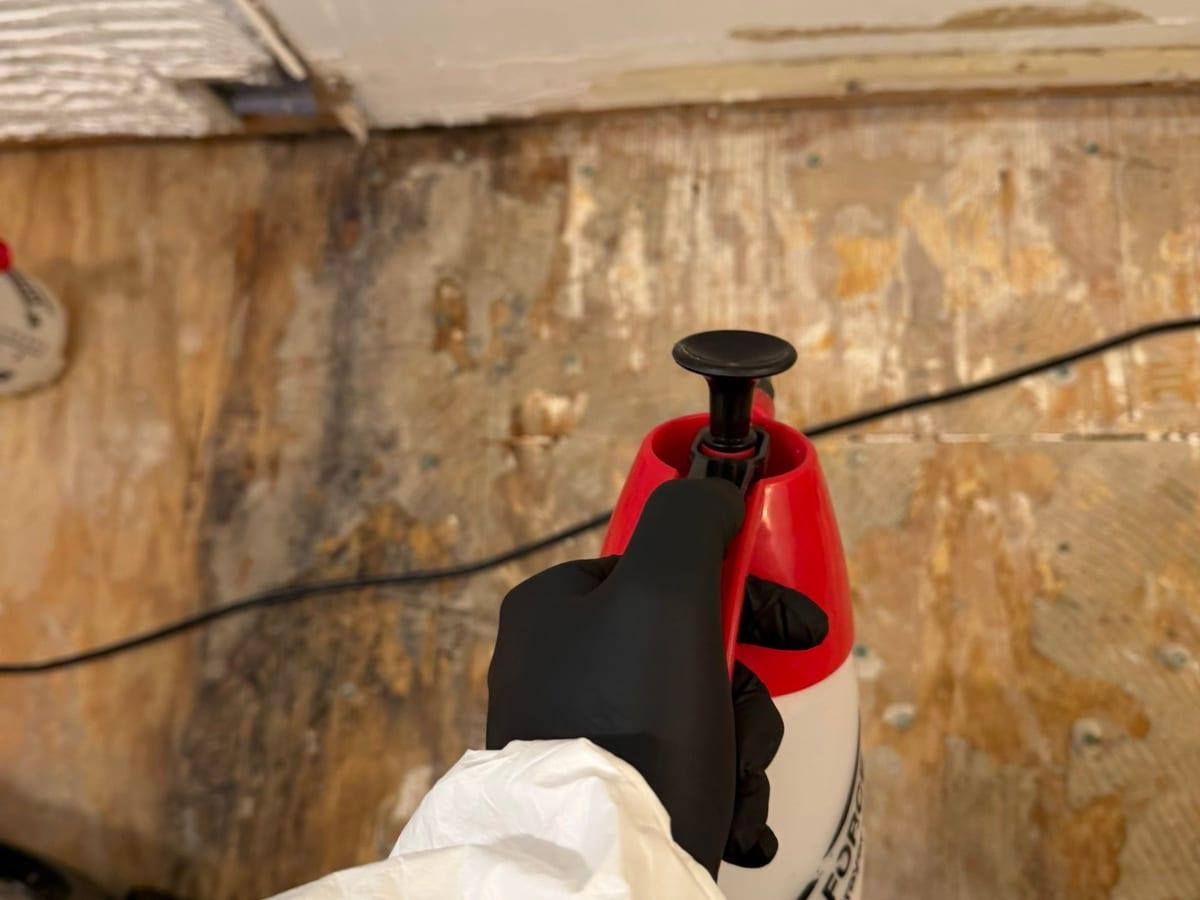 A technician in protective gear treating a damaged bathroom subfloor