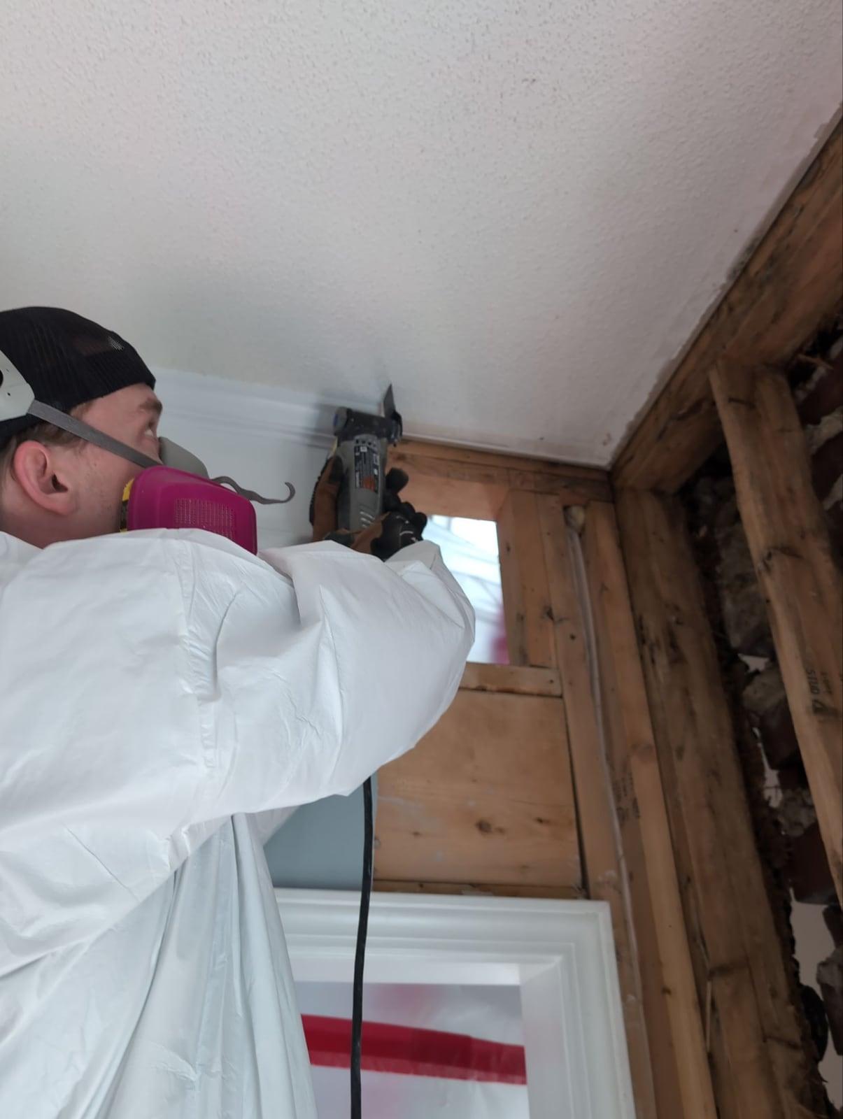 A technician in a respirator opening a wall to reach stained studs