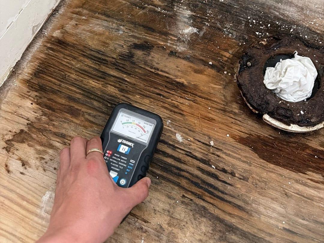 A moisture meter reading a water-stained wood floor