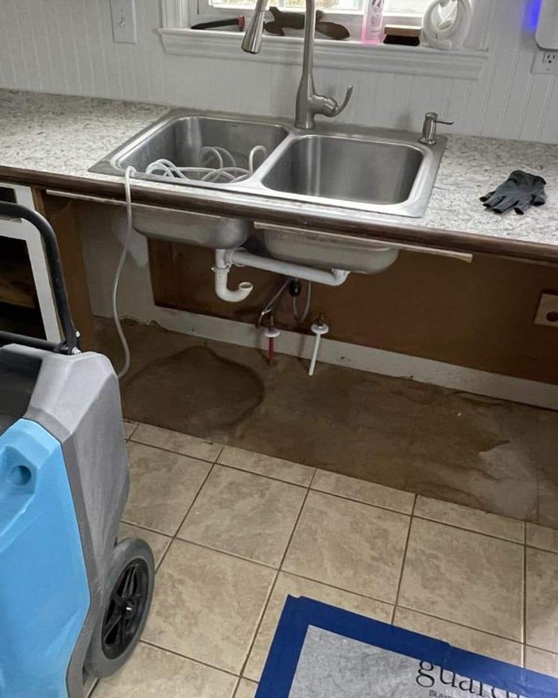 A kitchen sink cabinet removed and a dehumidifier drying the area after a leak