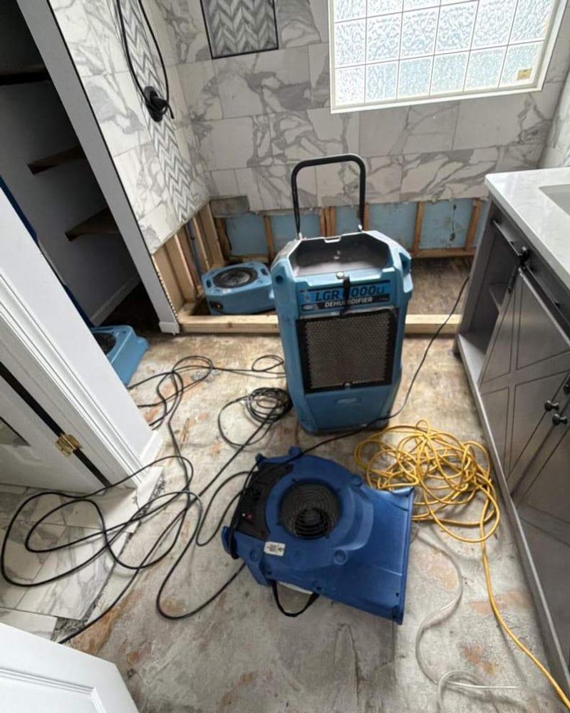 Air movers and a dehumidifier drying a bathroom after the shower was torn out