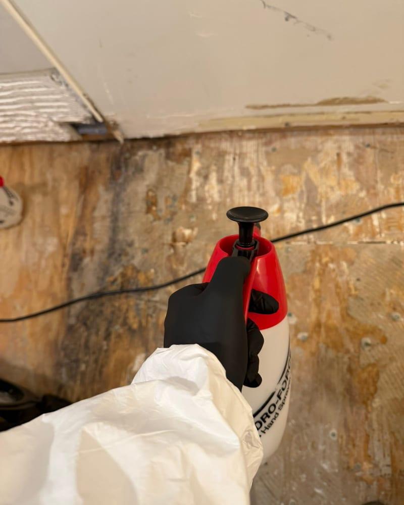 A technician in protective gear cleaning a bathroom subfloor after the flooring came out